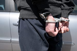 Close-up of a person in handcuffs standing near a car, representing legal assistance for criminal charges in Toronto.