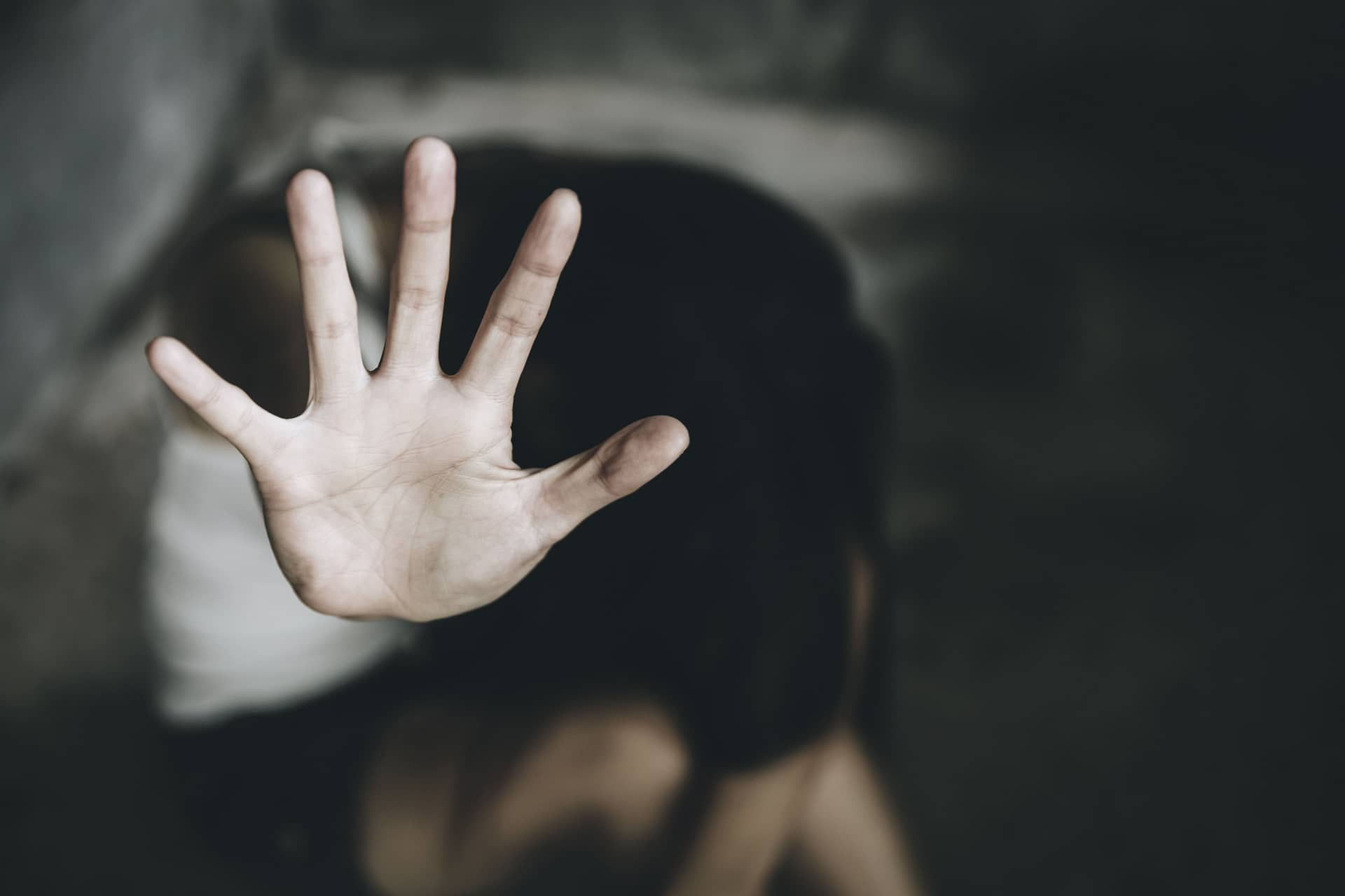 A person raising their hand in a defensive gesture, symbolizing protection or resistance, with a blurred background depicting vulnerability.