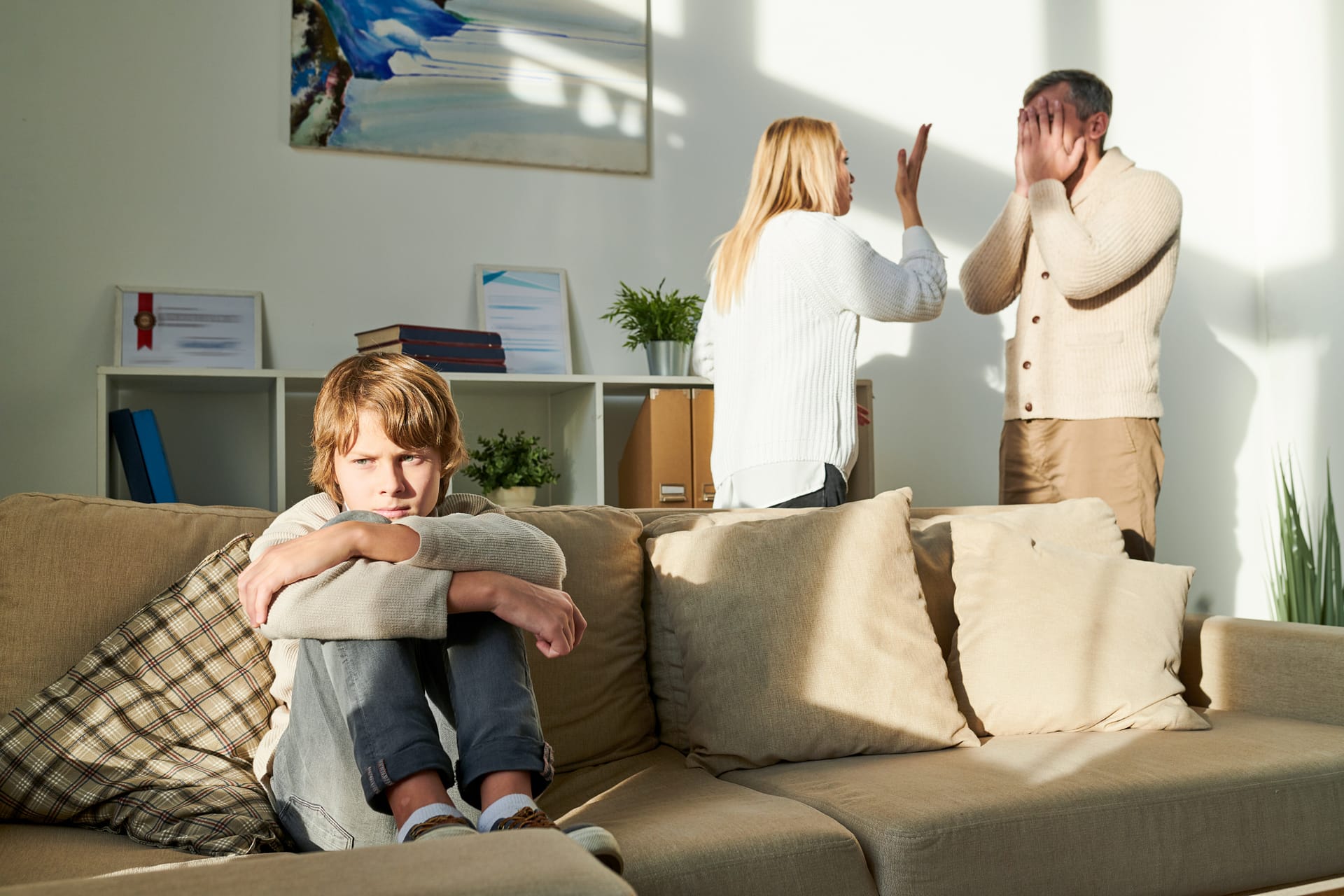 Sad child sitting on a couch while parents argue in the background, depicting family law issues in Toronto, Ontario, such as custody disputes or divorce.